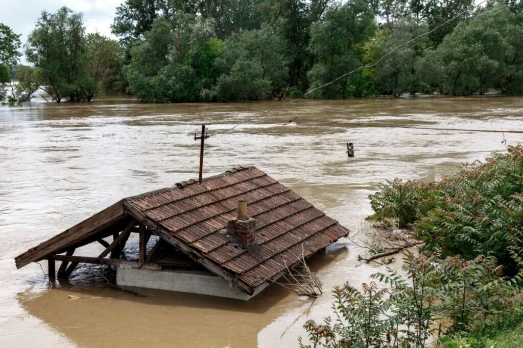 Toit submergé par les eaux dans une zone inondée, entouré d'arbres et de végétation, illustrant les zones vulnérables aux inondations en Belgique.